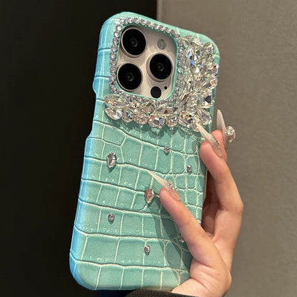 Turquoise phone case with crocodile texture and decorative elements held by a hand against a dark background