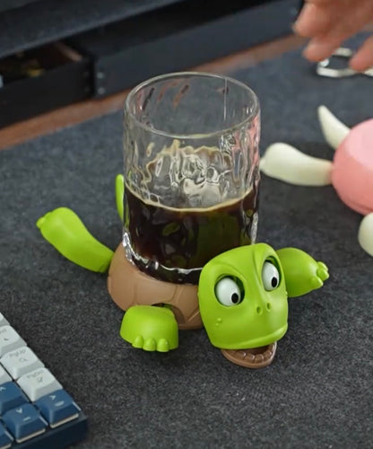 Green turtle-shaped glass holder with a glass of dark liquid on a desk.