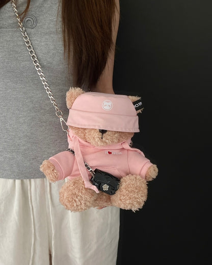 Teddy bear in a pink outfit with a matching bag held by a person against a black background