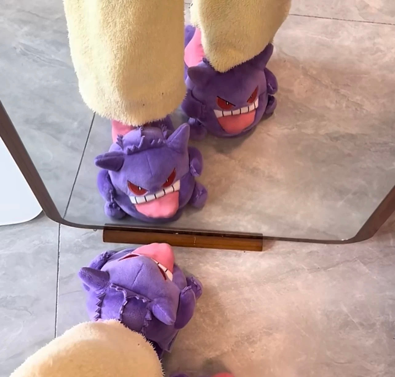 Purple slippers with cartoon face design worn by a person on a glass table.