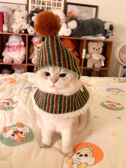 Cat wearing a striped hat with a pom-pom in a room with stuffed animals.