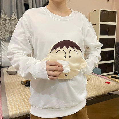 Person wearing a white sweatshirt with a cartoon character holding a tissue in a casual indoor setting.