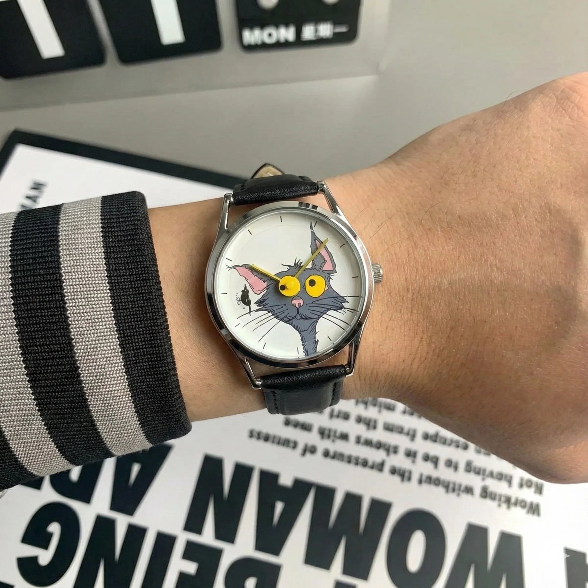 Wrist wearing a watch with a cat face design on a surface with text.
