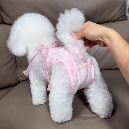 White dog wearing a pink outfit on a brown couch